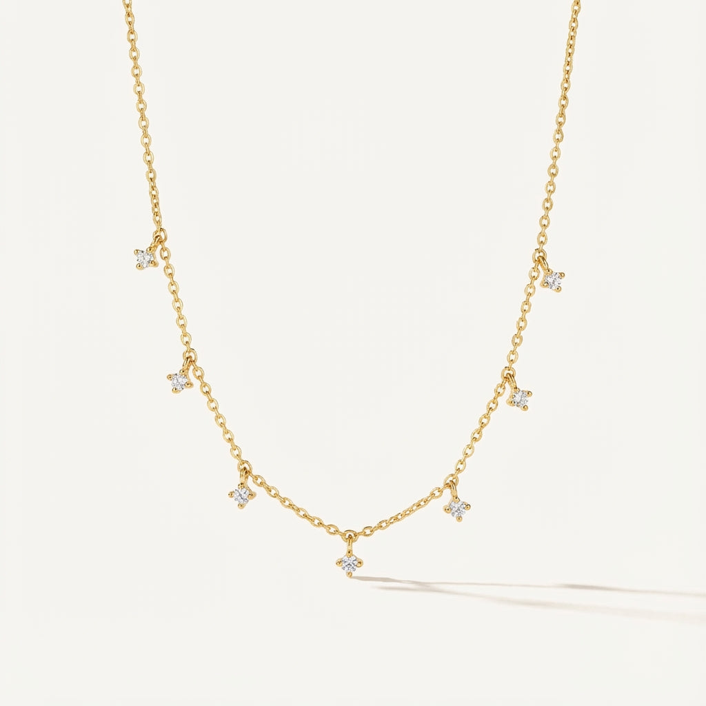 Golden plated silver necklace with square cubic zirconia dangle stones on a delicate chain, grey wood background.