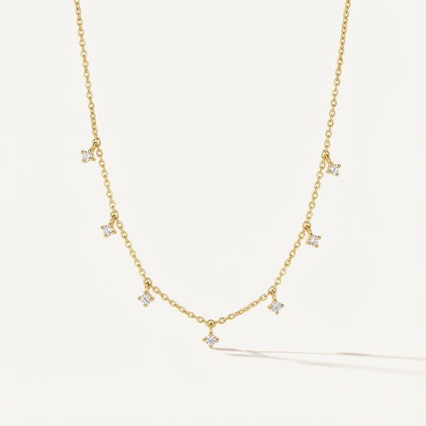 Golden plated silver necklace with square cubic zirconia dangle stones on a delicate chain, grey wood background.