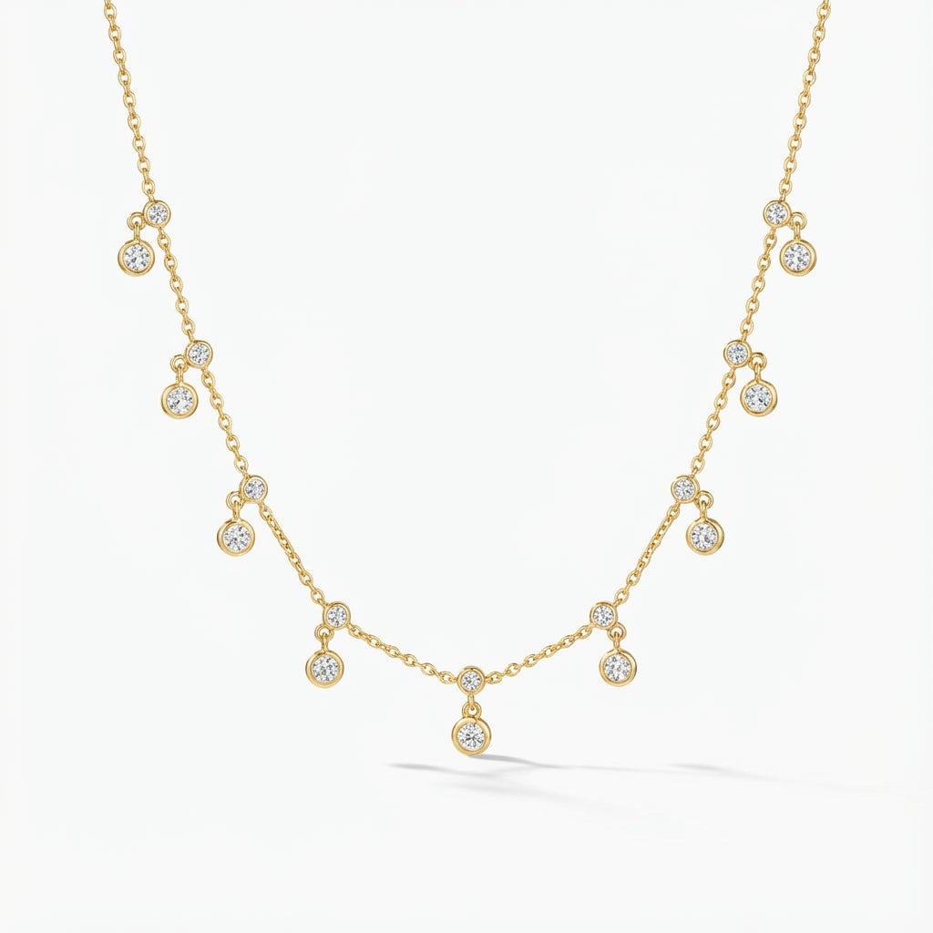 Golden plated silver delicate chain necklace with small sparkling double dangle charms, lying on a grey wooden surface.