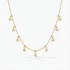 Golden plated silver delicate chain necklace with small sparkling double dangle charms, lying on a grey wooden surface.