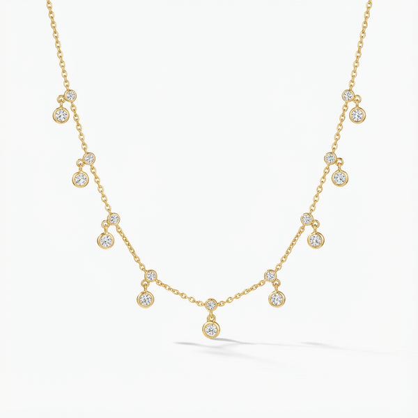 Golden plated silver delicate chain necklace with small sparkling double dangle charms, lying on a grey wooden surface.